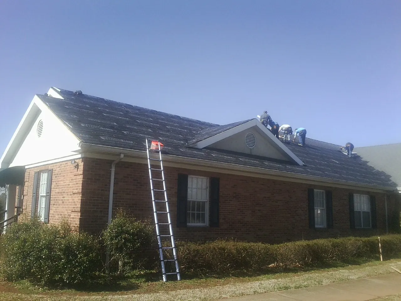 Crew tearing shingles off a brick ranch roof with a ladder set — Metal Roof Repair work by our crew in Gold Canyon