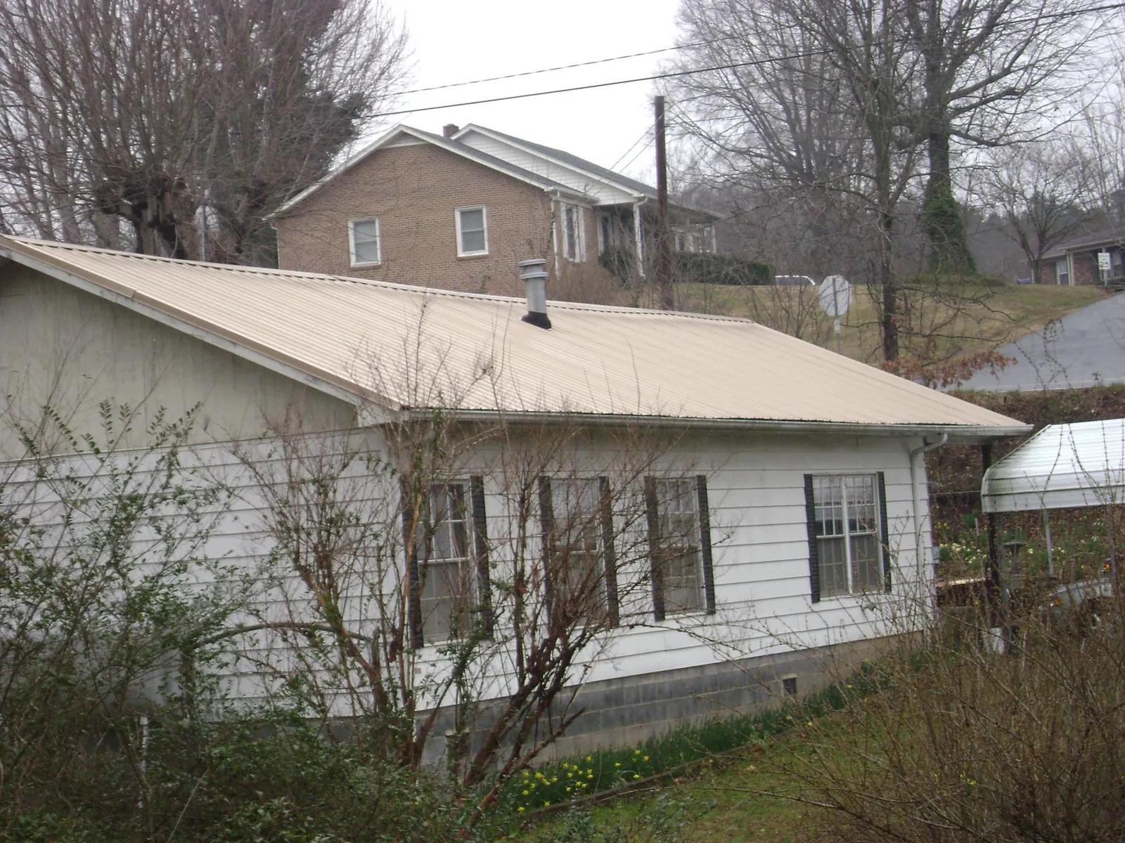 Tan metal roof on a white sided house set into a hillside — Commercial Roofing by Roofing Brothers in Gold Canyon